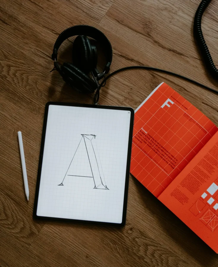 Graphic Design A pair of headphones, An ipad, an apple pencil and an orange design book.